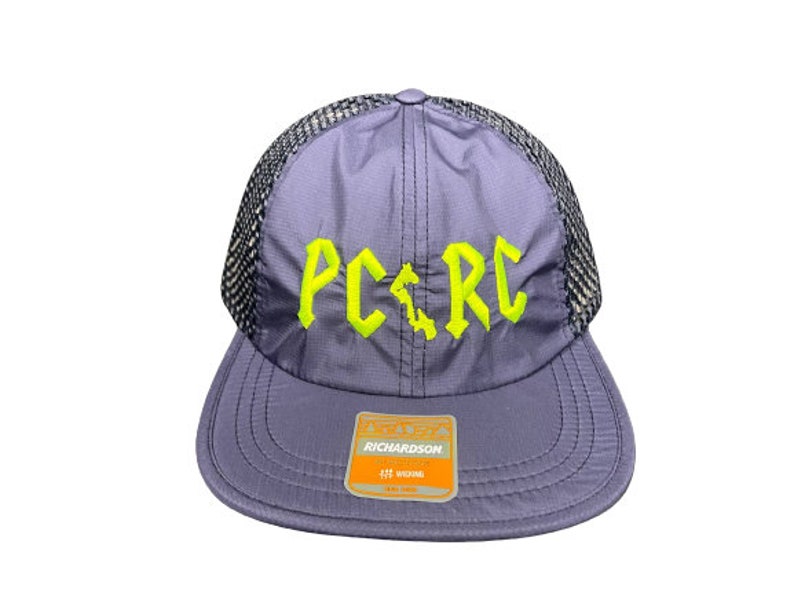 May include: A lavender baseball cap with a black mesh back and a flat brim. The front features the neon yellow embroidered text PC RC with a small vertical shape between the letters. A rectangular Richardson brand sticker is on the brim.