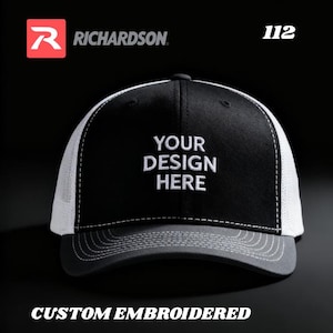 Könnte beinhalten: Schwarz-weiße Trucker-Cap mit dem Text "YOUR DESIGN HERE" weiß gestickt. Die Kappe hat einen grauen Schirm und eine weiße Mesh-Rückseite. Das Richardson-Logo ist sichtbar.