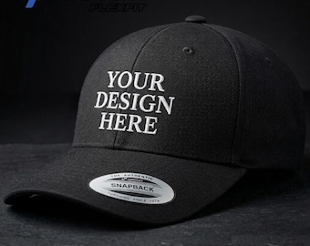 May include: A black baseball cap featuring the white embroidered text YOUR DESIGN HERE on the front crown. The cap includes a Yupoong Flexfit logo, a 5789m model number, and a circular silver and black sticker on the brim reading THE AUTHENTIC SNAPBACK.