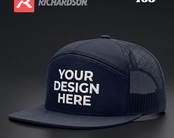 May include: A navy blue trucker hat featuring a flat brim and a mesh back panel. The front panel displays the white embroidered text YOUR DESIGN HERE. The Richardson logo and the number 168 are visible in the upper corners, with CUSTOM EMBROIDERED text below.