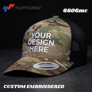 Puede incluir: Gorra de béisbol con estampado de camuflaje y parte trasera de malla negra. La parte delantera de la gorra presenta el texto "YOUR DESIGN HERE" en bordado blanco. La gorra también tiene una visera curva y cierre snapback. El texto "CUSTOM EMBROIDERED" está en la parte inferior.