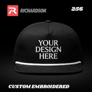 Puede incluir: Gorra de béisbol negra bordada a medida con texto blanco "YOUR DESIGN HERE". La gorra tiene un detalle de cuerda blanca a lo largo del borde. El logotipo de Richardson es visible en la esquina superior izquierda.