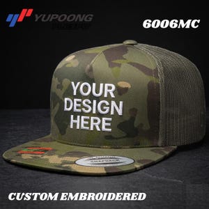May include: A camouflage print snapback cap with a mesh back and a flat brim. The front panel features the white embroidered text "YOUR DESIGN HERE". The cap includes a Yupoong Flexfit logo, the model number 6006MC, and a circular sticker on the brim.