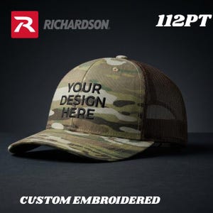 May include: Camouflage baseball cap with a brown mesh back. The cap features the text "YOUR DESIGN HERE" in black, and the words "CUSTOM EMBROIDERED" are at the bottom. The Richardson logo is in the top left corner.