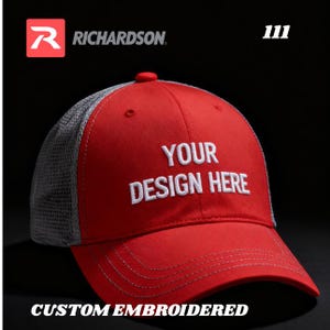 May include: A red and gray trucker hat with the text "YOUR DESIGN HERE" embroidered in white. The hat features the Richardson logo and the words "CUSTOM EMBROIDERED".