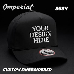 Puede incluir: Gorra de béisbol negra con el texto blanco bordado "YOUR DESIGN HERE". La gorra tiene una visera curva y una etiqueta "TRUE FIT". La palabra "Imperial" está encima de la gorra. Las palabras "CUSTOM EMBROIDERED" están en la parte inferior.
