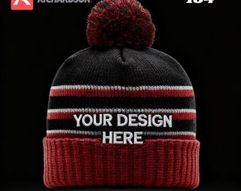 Può includere: Un berretto lavorato a maglia nero e rosso con un pompon. Il cappello presenta strisce bianche e rosse e il testo "YOUR DESIGN HERE". La fascia inferiore è rossa e il testo "CUSTOM EMBROIDERED" è in basso.