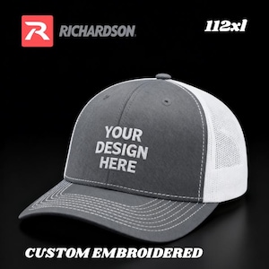 May include: Gray and white trucker hat with the text "YOUR DESIGN HERE" embroidered on the front. The hat has a curved brim and a mesh back. The Richardson logo is visible in the upper left corner. The text "CUSTOM EMBROIDERED" is at the bottom.