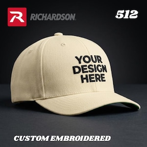 May include: A beige baseball cap with a curved brim. The cap features the text "YOUR DESIGN HERE" in black, and the words "CUSTOM EMBROIDERED" are at the bottom. The Richardson logo is visible.