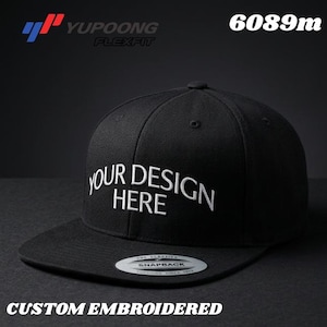 Puede incluir: Gorra de béisbol negra Flexfit con el texto "YOUR DESIGN HERE" bordado en blanco. La gorra también presenta el texto "CUSTOM EMBROIDERED" y el nombre de la marca "Yupoong Flexfit".