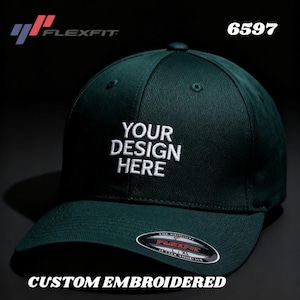 Peut inclure: Casquette de baseball Flexfit vert foncé avec le texte "YOUR DESIGN HERE" brodé en blanc. La casquette présente également le logo Flexfit et le texte "CUSTOM EMBROIDERED".