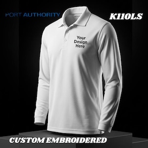 May include: White long-sleeve polo shirt with a collar and three-button placket. The shirt features the text "Your Design Here" embroidered on the chest. The image also displays the text "PORT AUTHORITY", "K110LS", and "CUSTOM EMBROIDERED".