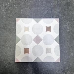 May include: Square tile featuring a repeating pattern of circles, squares, and diamond shapes in grey, pink, and brown. The tile has a light grey background, suitable for flooring or wall applications.