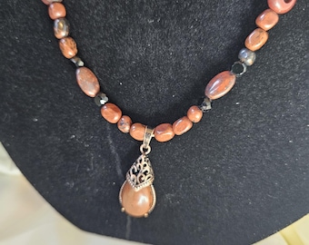 Röd koppar med hänge i röd jaspis och ovala, små pärlor i jaspis. Svarta myntkristaller.