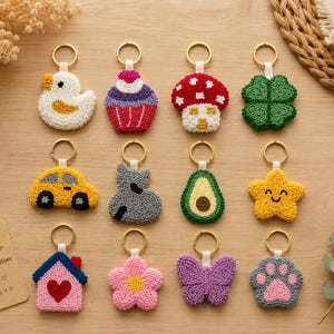 May include: A collection of twelve punch needle keychains featuring various shapes including a white duck, cupcake, red mushroom, green clover, yellow car, grey cat, avocado, yellow star, house, pink flower, purple butterfly, and a paw print.