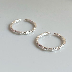 Könnte beinhalten: Zwei silberne Ohrringe mit einem strukturierten, geflochtenen Design. Die Ohrringe liegen auf einem weißen Teller.