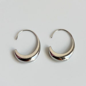 May include: A pair of silver hoop earrings with a curved, rounded shape.