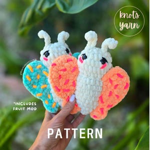 May include: Crocheted butterfly pattern in white, orange, and turquoise. The butterflies have black eyes and pink cheeks. The word "PATTERN" is at the bottom of the image, and the text "*INCLUDES FRUIT MOD" is also visible.