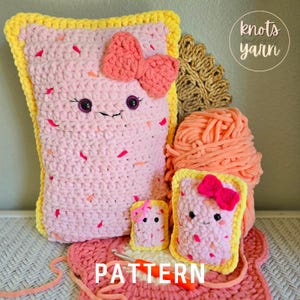 May include: A collection of handmade crochet items, including a large pink pillow and two smaller pieces, all resembling a smiling pastry with a bow. The items have yellow borders and are decorated with pink and orange sprinkles. The word "PATTERN" is visible.