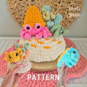 May include: A collection of crocheted plush toys including a pink crab with an orange hat, a yellow axolotl, and a blue dinosaur. The items are textured with soft yarn and feature black plastic eyes. The text "knots merry yarn" and "PATTERN" appear.