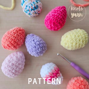 May include: A collection of colorful crocheted Easter eggs in various shades of pink, purple, yellow, orange, and white. The eggs are made with fluffy yarn and have a textured surface. The image also includes a crochet hook and the text "knots n'merry yarn".