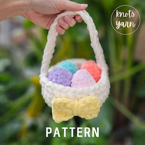 May include: A white crocheted Easter basket with a yellow bow, filled with colorful crocheted eggs. The basket is held by a hand and the text "knots yarn" is visible in the background.