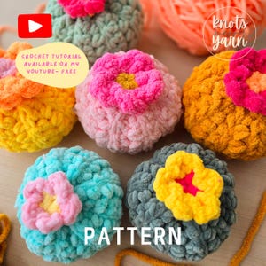 Peut inclure: Cinq boules crochetées en fil coloré avec des embellissements floraux. Les boules sont disposées en demi-cercle sur une surface en bois. Le texte "PATTERN" est écrit sous les boules. Le texte "CROCHET TUTORIAL AVAILABLE ON MY YOUTUBE - FREE" est écrit sur une icône de bouton de lecture dans le coin supérieur gauche de l'image.