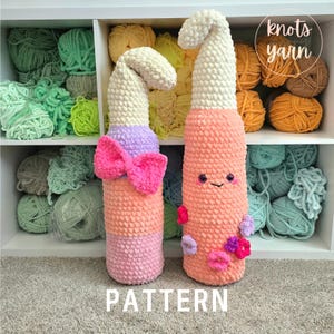 May include: Two handmade crochet gnome-like figures. One has a pink bow, the other has a smiling face and flower accents. The figures are peach, pink, and white. The word "PATTERN" is at the bottom.