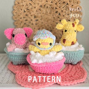 Peut inclure: Trois peluches crochetées dans de petites baignoires : un éléphant rose, un canard jaune avec un bonnet à fleurs et une girafe jaune. Chaque figurine est assise dans des bulles en laine blanche. Le mot PATTERN est écrit en blanc en bas.