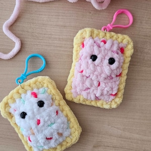 Puede incluir: Dos llaveros de ganchillo con forma de Pop-Tarts. Uno es rosa con chispas rojas y el otro es blanco con chispas rosas y verdes.