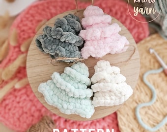 May include: Four crocheted Christmas tree ornaments in different colors: gray, pink, light blue, and white. The ornaments are arranged on a wooden surface with the text "PATTERN" below them.