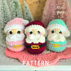 May include: Three crocheted Santa Claus figures in pink, red, and teal, each with a white beard and hat. The figures have black eyes and pink cheeks. The word "PATTERN" is visible on a pink crocheted surface.
