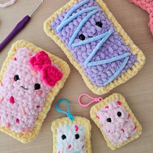 Puede incluir: Cuatro juguetes de peluche tejidos a crochet con forma de Pop-Tarts con rellenos de diferentes colores. Los juguetes tienen caras sonrientes y est&aacute;n hechos con una variedad de colores, incluyendo rosa, morado, azul y blanco.