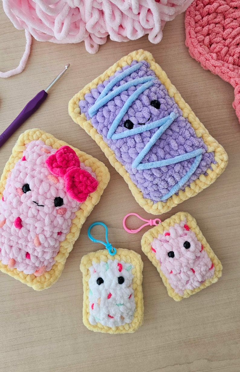 Puede incluir: Cuatro juguetes de peluche tejidos a crochet con forma de Pop-Tarts con rellenos de diferentes colores. Los juguetes tienen caras sonrientes y est&aacute;n hechos con una variedad de colores, incluyendo rosa, morado, azul y blanco.