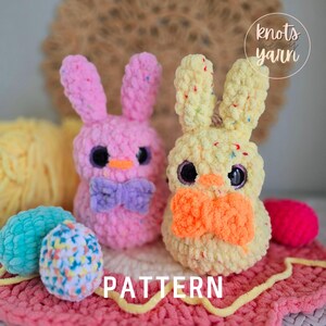 May include: Two crocheted Easter bunny plushies, one pink with a purple bow and one yellow with an orange bow. The bunnies are sitting on a pink and yellow crocheted surface. The text "knots yarn" is visible in the upper right corner of the image. The text "PATTERN" is visible in the lower center of the image.