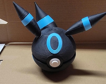 May include: A black and blue 3D printed Pokemon figure of a Darkrai. The figure has three black spikes with blue stripes and a white button on the front.