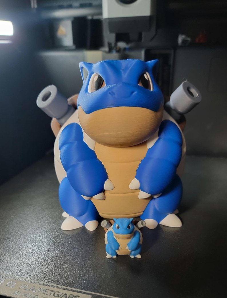 May include: A blue and brown 3D printed figurine of a Pokemon character, Squirtle, standing next to a larger version of the same character, Blastoise.