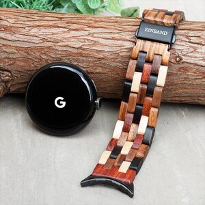 Puede incluir: Una correa de reloj de madera con un patrón multicolor. La correa está hecha de diferentes tipos de madera, incluyendo marrón claro, marrón oscuro y negro. La correa tiene una hebilla de metal negro con la palabra "EINBAND" impresa en ella.