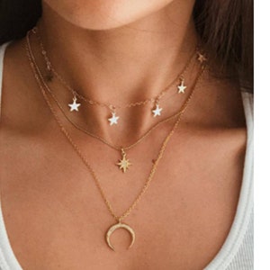 May include: A layered gold necklace with a crescent moon pendant and star charms.