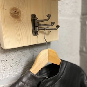 May include: A black leather jacket hanging on a wooden shelf with a metal hook. The hook is attached to the shelf with a hinge.