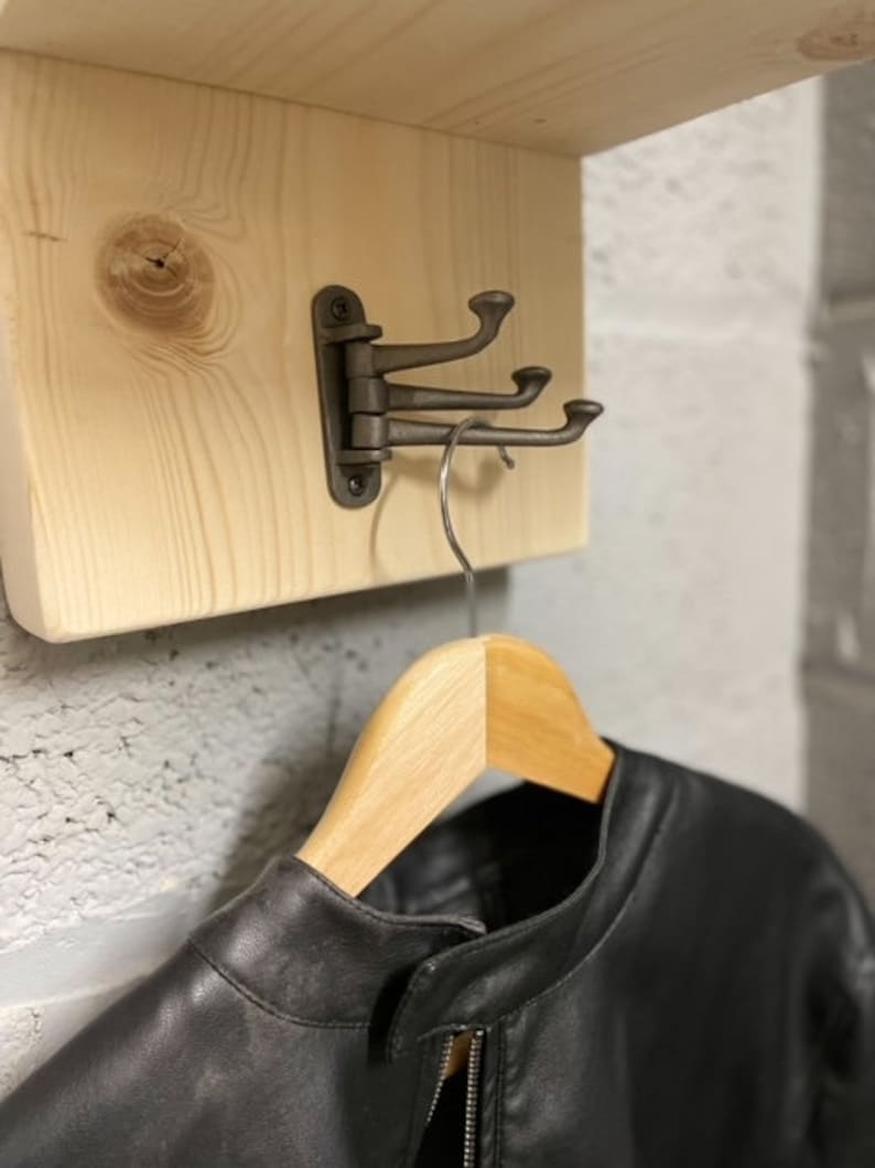 May include: A black leather jacket hanging on a wooden shelf with a metal hook. The hook is attached to the shelf with a hinge.