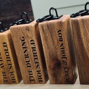 May include: A set of eight wooden doorstops with black metal rings. Each doorstop is engraved with a different name, including "The Tindele Household", "Thomas", "The Avill Household", "The Durning Household", "Juney & John Boy", "Ryan & Lucy", and "The Jordans".