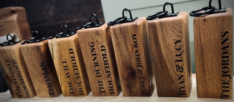 May include: A set of eight wooden doorstops with black metal rings. Each doorstop is engraved with a different name, including "The Tindele Household", "Thomas", "The Avill Household", "The Durning Household", "Juney & John Boy", "Ryan & Lucy", and "The Jordans".