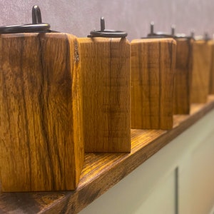 May include: A row of wooden candle holders with black metal rings on top. The holders are arranged on a wooden shelf.