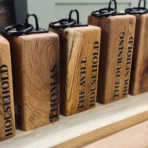 May include: A row of wooden doorstops with black metal rings and personalised names, including "The Tindell Household", "Thomas", "The Avell Household", "The Durning Household", "Junky & John Boy", "Ivan & Lucy", and "Luf Jordans".