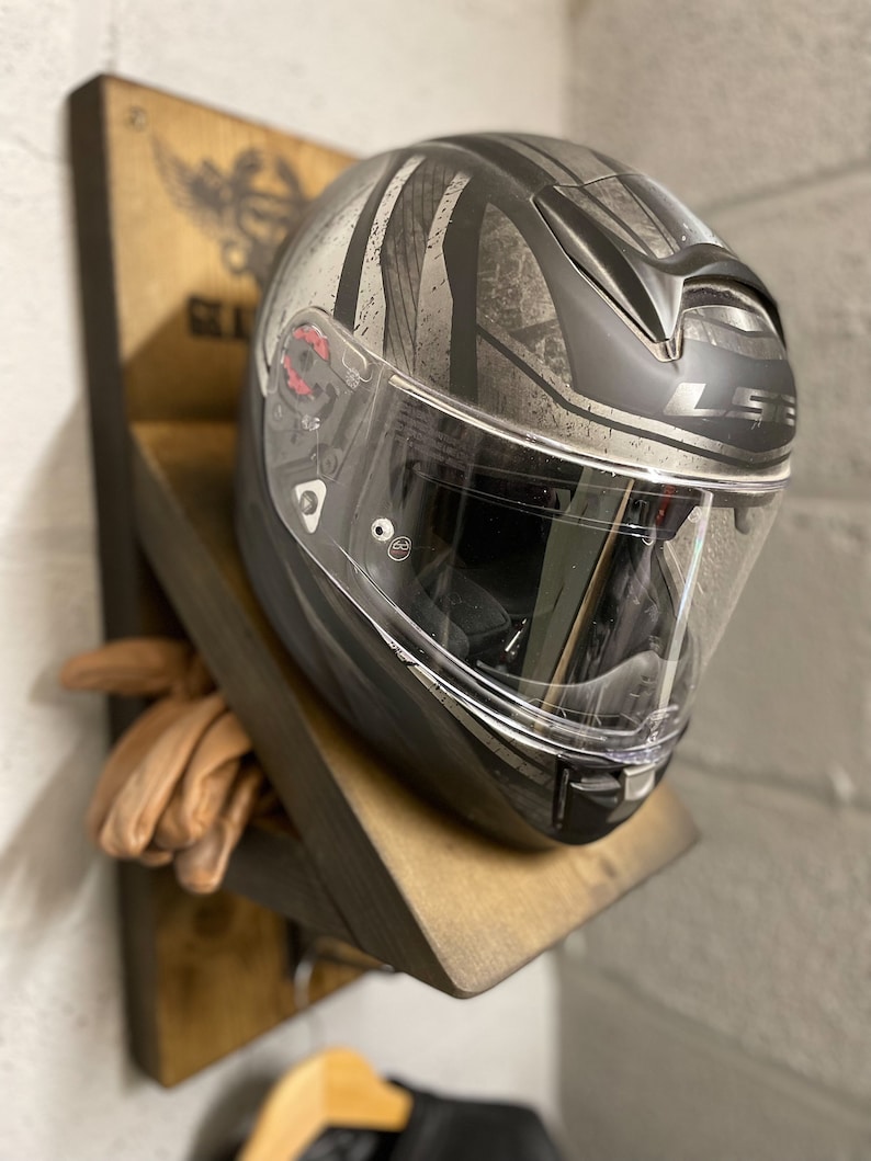 May include: A wooden helmet holder with a grey and white motorcycle helmet hanging on it. The helmet has a clear visor and a black and white design.