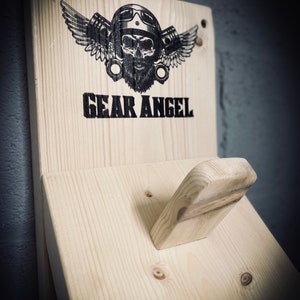 May include: A wooden wall mount with a skull wearing a helmet and wings, with the text "GEAR ANGEL" printed below. The mount has a small wooden hook on the right side.