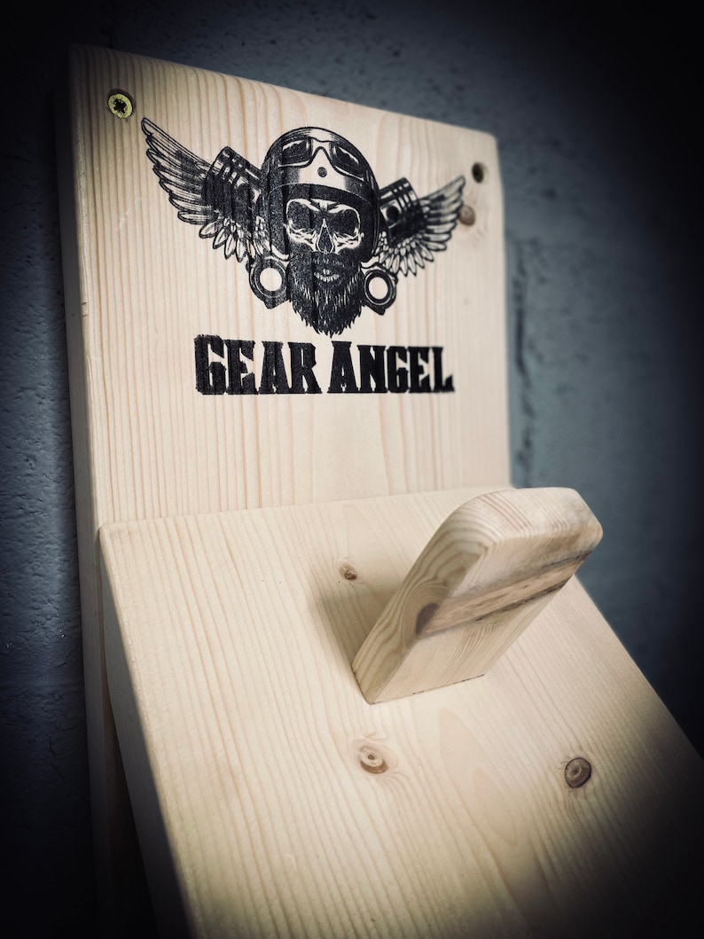 May include: A wooden wall mount with a skull wearing a helmet and wings, with the text "GEAR ANGEL" printed below. The mount has a small wooden hook on the right side.