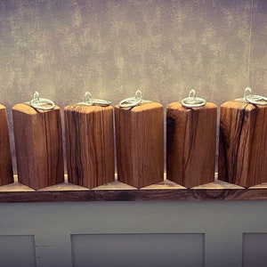 May include: A row of 11 wooden keychains with silver rings. The keychains are made of natural wood with a rustic finish. They are arranged on a wooden shelf.