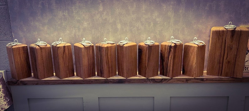 May include: A row of 11 wooden keychains with silver rings. The keychains are made of natural wood with a rustic finish. They are arranged on a wooden shelf.